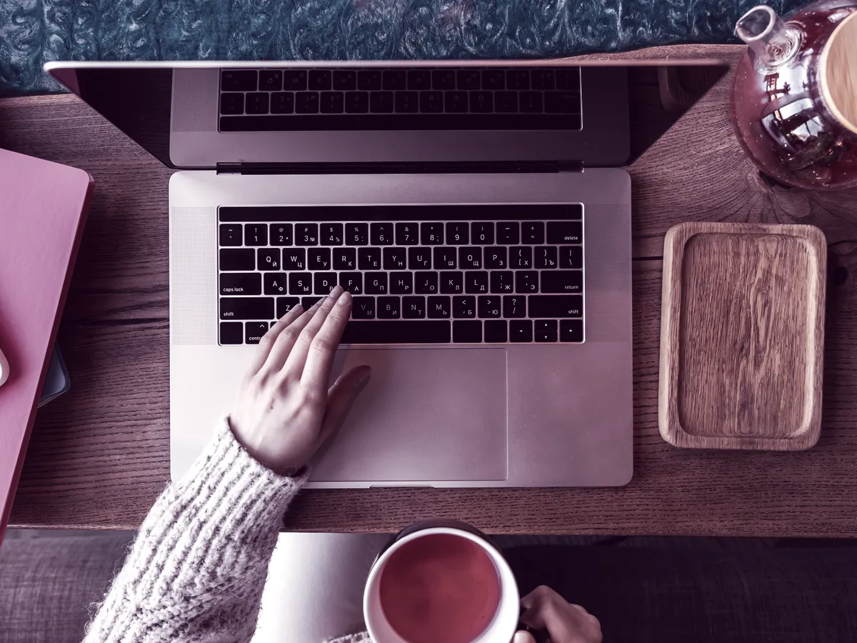 Pessoa escrevendo no notebook com uma xícara de chá, vista de cima